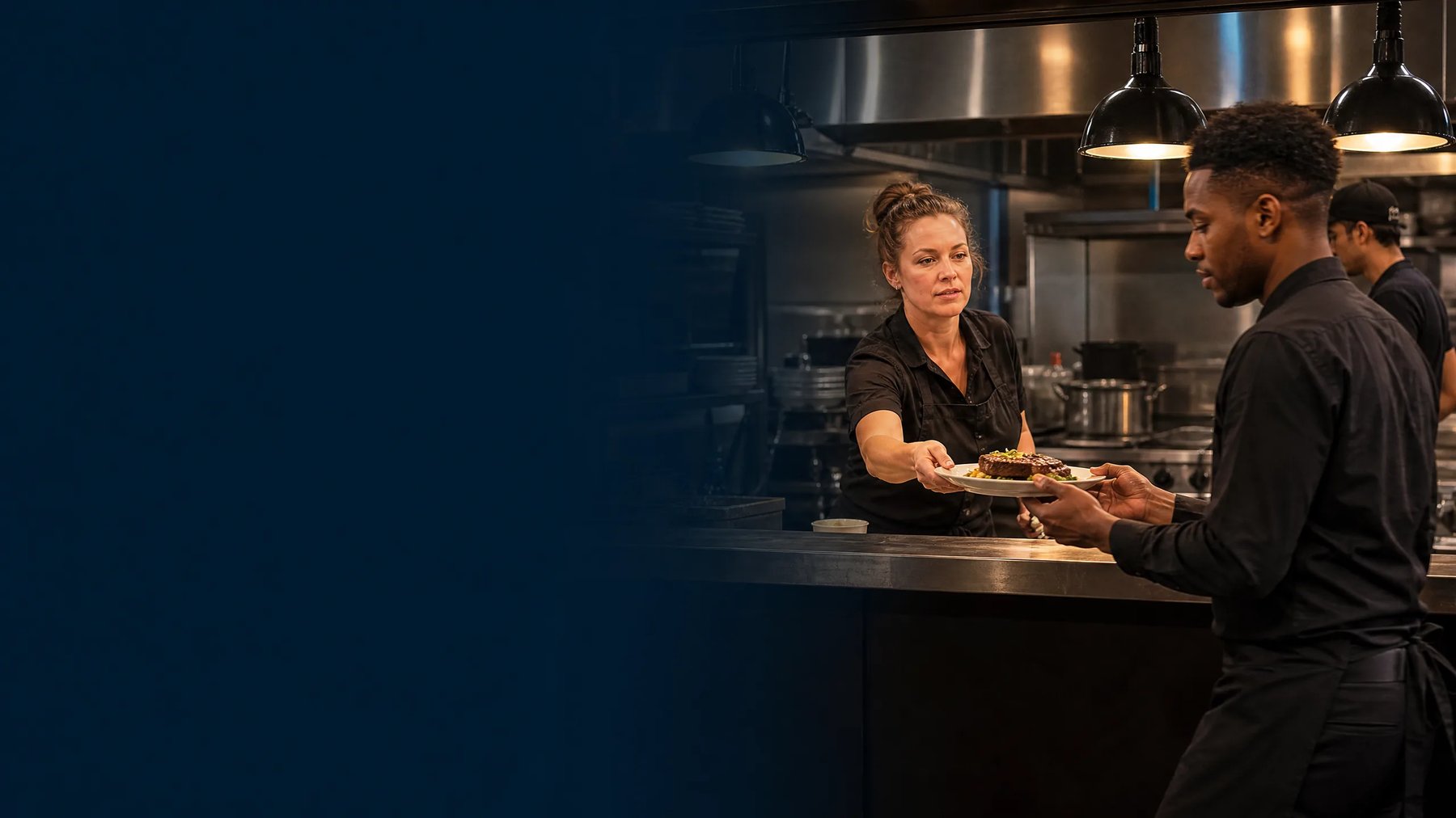 A restaurant owner and server coordinating dinner service in a professional kitchen